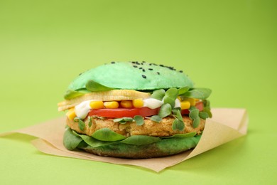 Photo of Tasty vegan burger with vegetables, patty and microgreens on green background, closeup