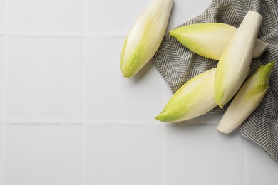 Photo of Fresh raw Belgian endives (chicory) on white tiled table, top view. Space for text