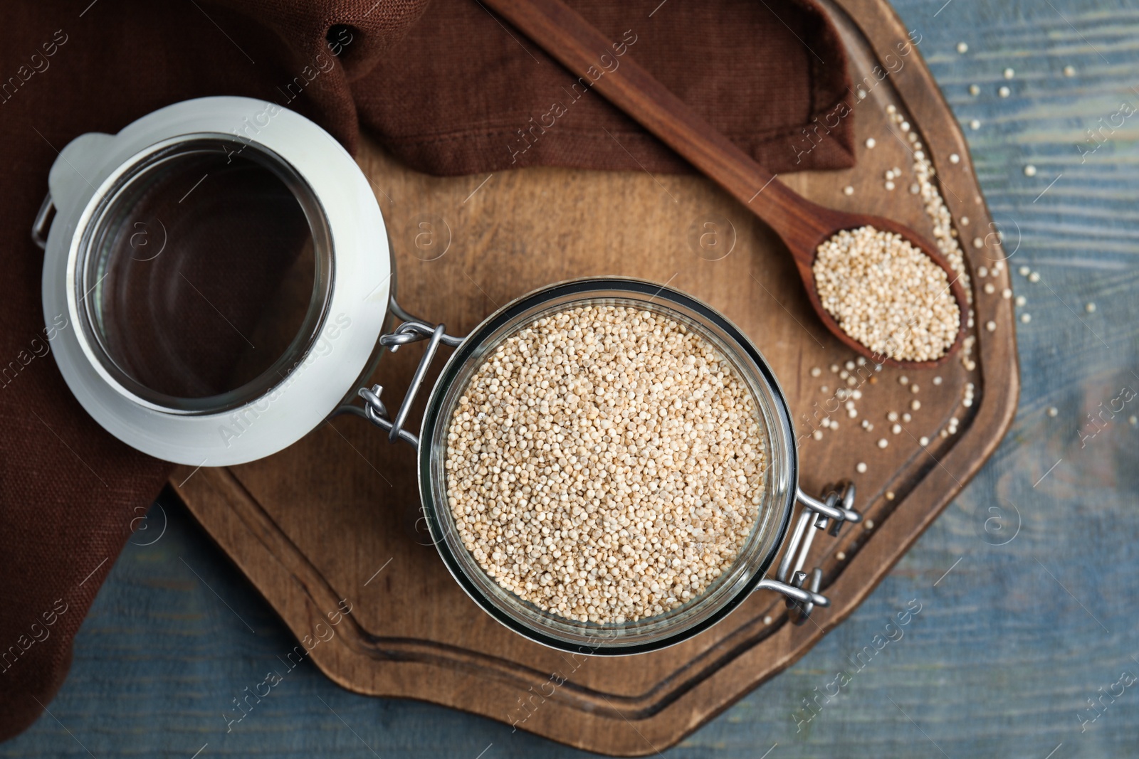 Photo of Jar and spoon with white quinoa on blue wooden table, flat lay