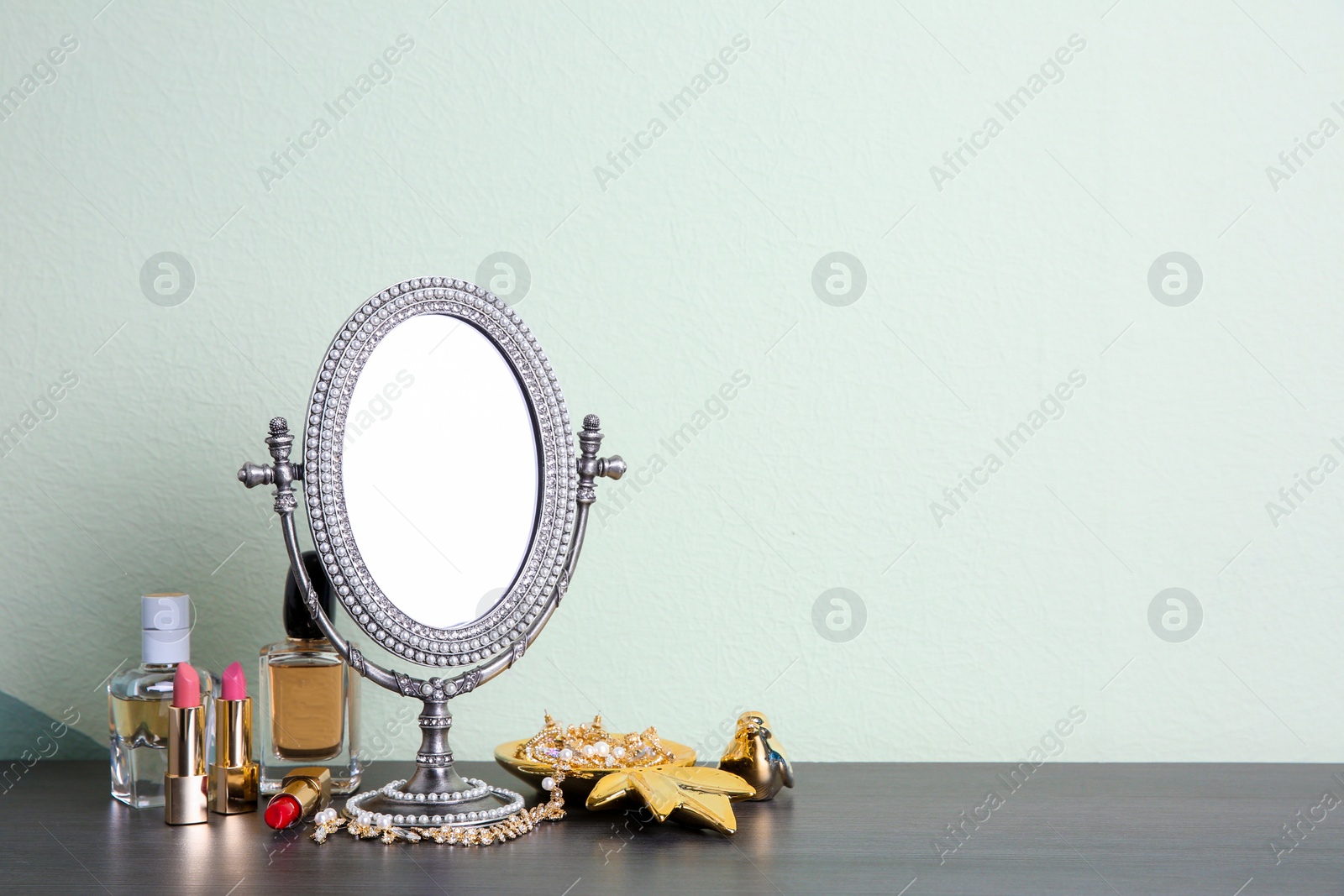 Photo of Stylish mirror, makeup products and accessories on table near light wall