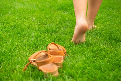 Photo of Woman leaving her shoes and walking away barefoot on green grass, closeup