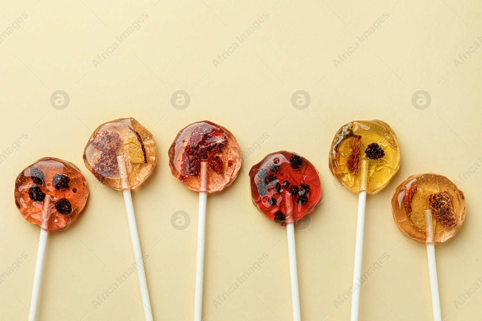 Photo of Sweet colorful lollipops with berries on beige background, flat lay