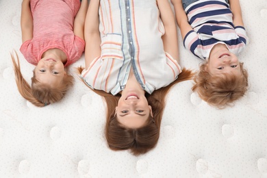 Photo of Mother and her children lying on new orthopedic mattress, top view