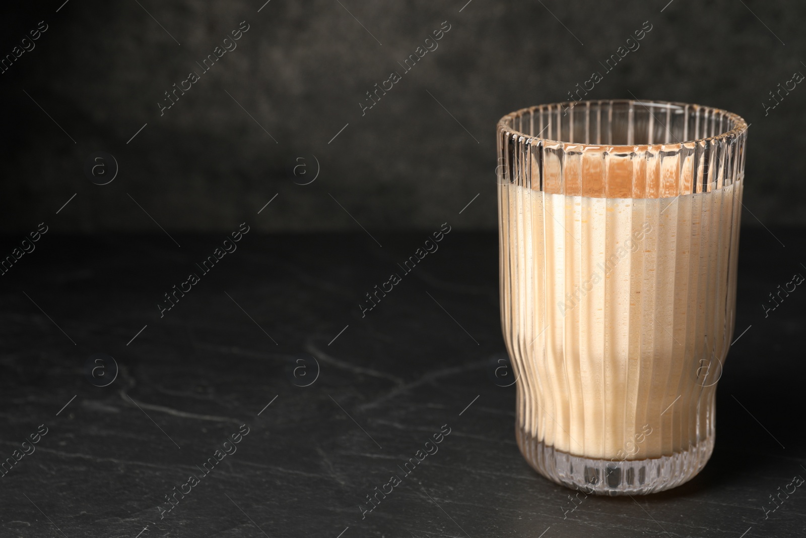 Photo of Glass of delicious eggnog on black marble table. Space for text