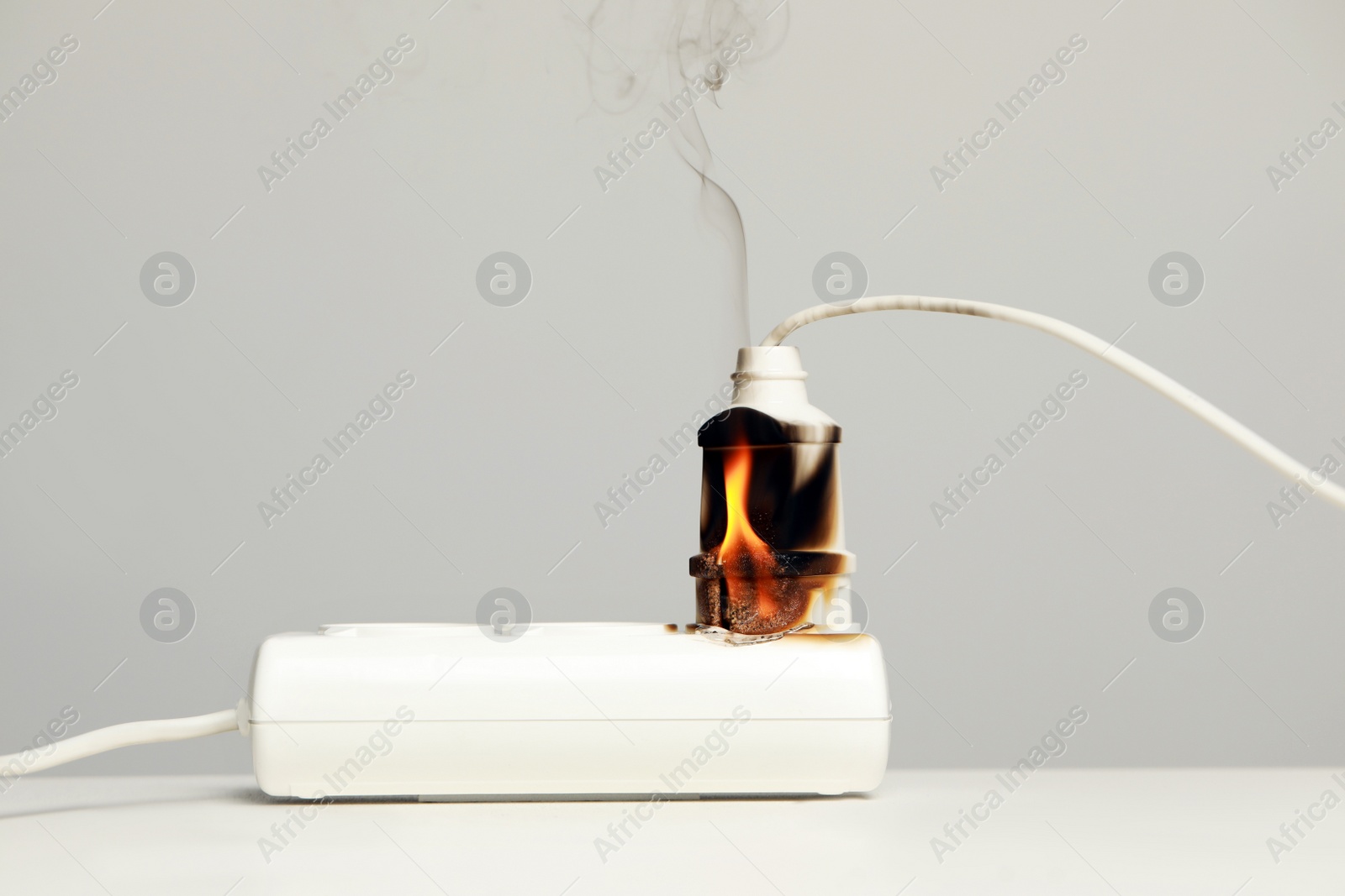 Photo of Inflamed plug in power strip on white table against grey wall. Electrical short circuit