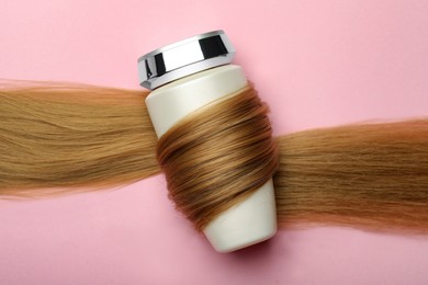Photo of Bottle wrapped in lock of hair on pink background, top view. Natural cosmetic product