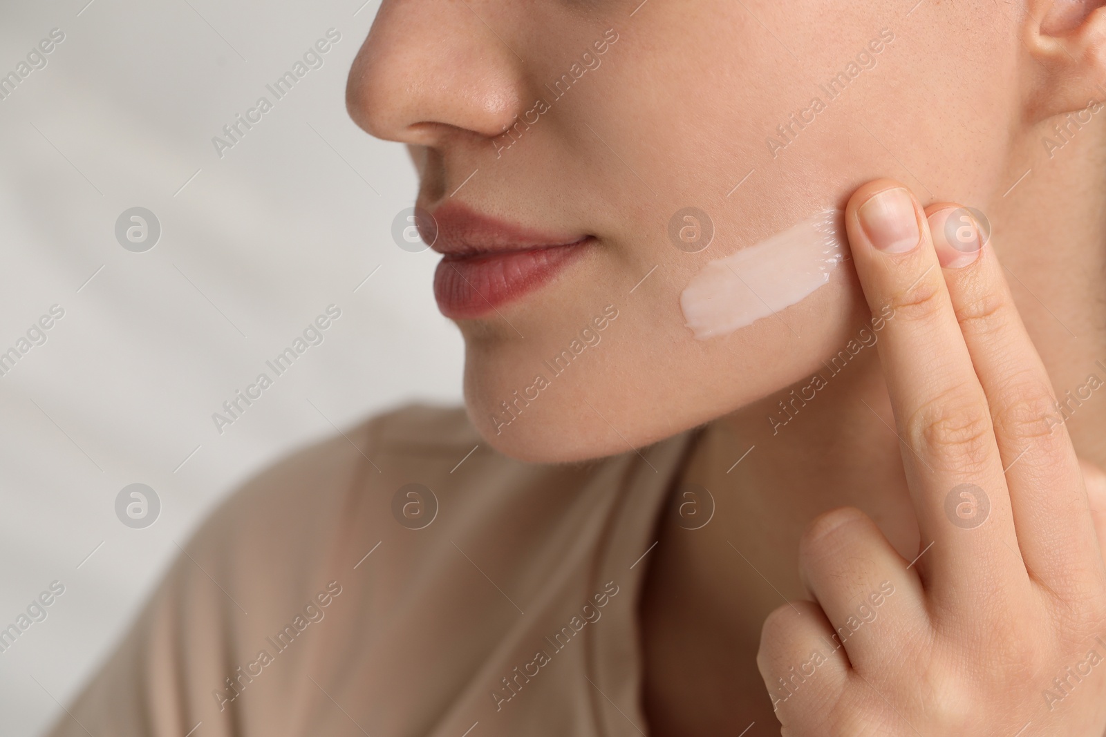 Photo of Young woman with dry skin applying cream onto her face on blurred background, closeup