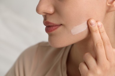 Photo of Young woman with dry skin applying cream onto her face on blurred background, closeup