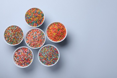 Photo of Colorful sprinkles in bowls on light grey background, flat lay with space for text. Confectionery decor