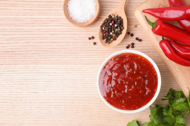 Photo of Bowl of hot chili sauce with ingredients on wooden background, flat lay. Space for text