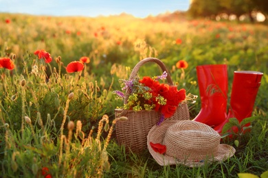 Photo of Basket of wildflowers with straw hat and boots in sunlit poppy field