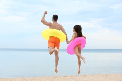 Happy young couple having fun with inflatable rings on beach near sea