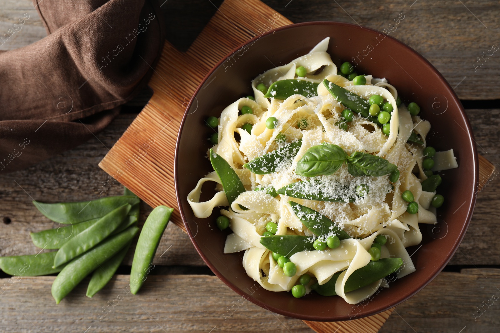 Photo of Delicious pasta with green peas, fresh basil and cheese on wooden table, flat lay