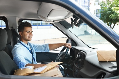 Young courier with parcels in delivery car