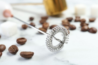 Photo of Milk frother wand and coffee beans on white marble table, closeup