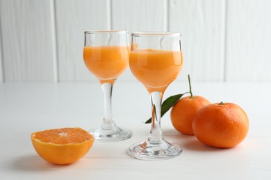 Photo of Tasty tangerine liqueur in glasses and fresh citrus fruits on white table