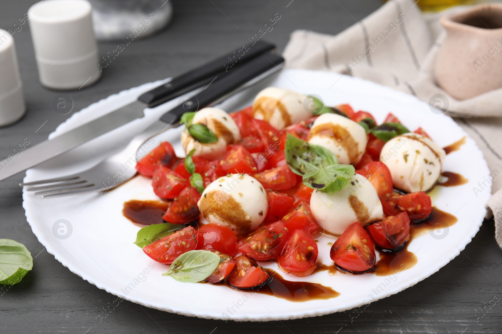 Photo of Tasty salad Caprese with tomatoes, mozzarella balls, basil and balsamic vinegar on grey table, closeup