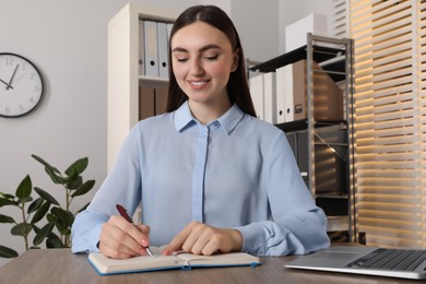 Photo of Happy woman taking notes at wooden table in office