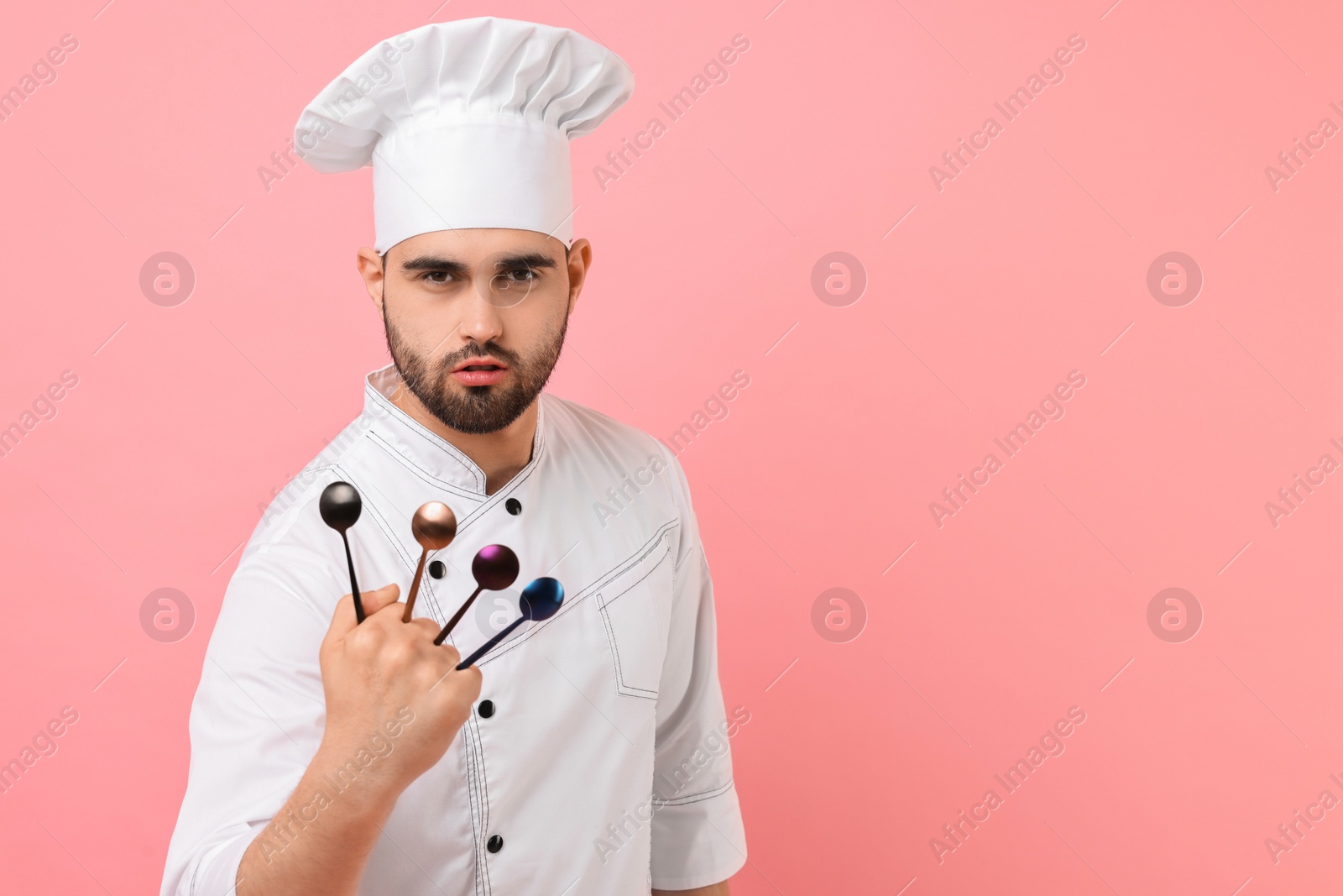 Photo of Professional chef holding kitchen utensils on pink background. Space for text