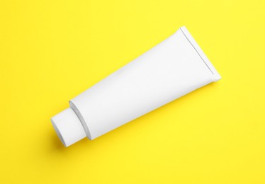 Photo of Blank white tube of ointment on yellow background, top view. Space for text