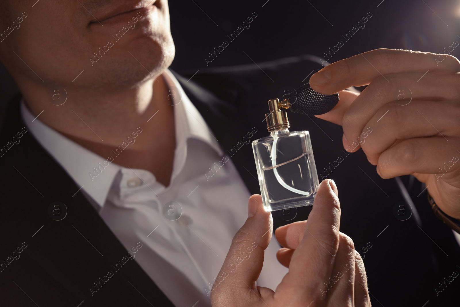 Photo of Handsome man applying perfume on neck against black background, closeup