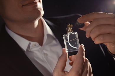 Photo of Handsome man applying perfume on neck against black background, closeup
