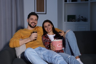 Photo of Happy couple with popcorn watching TV at home in evening