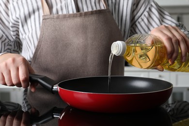 Woman pouring cooking oil from bottle into frying pan on stove, closeup