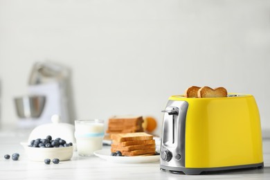 Photo of Yellow toaster with roasted bread slices, blueberries and glass of milk on white marble table