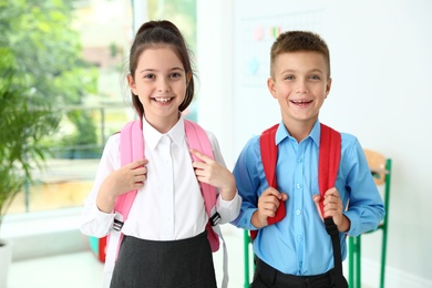 Photo of Cute little children with backpacks in classroom at school