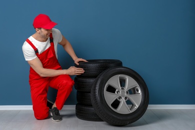 Young mechanic sitting near car tires near color wall