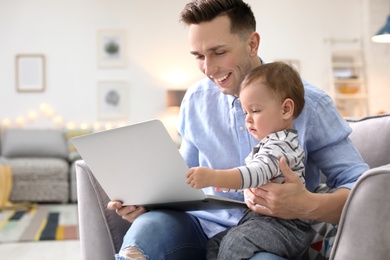 Young father with his cute little son using laptop at home