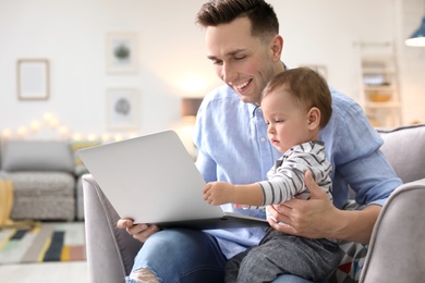 Photo of Young father with his cute little son using laptop at home