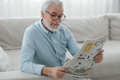 Portrait of grandpa with stylish glasses reading newspaper on sofa indoors