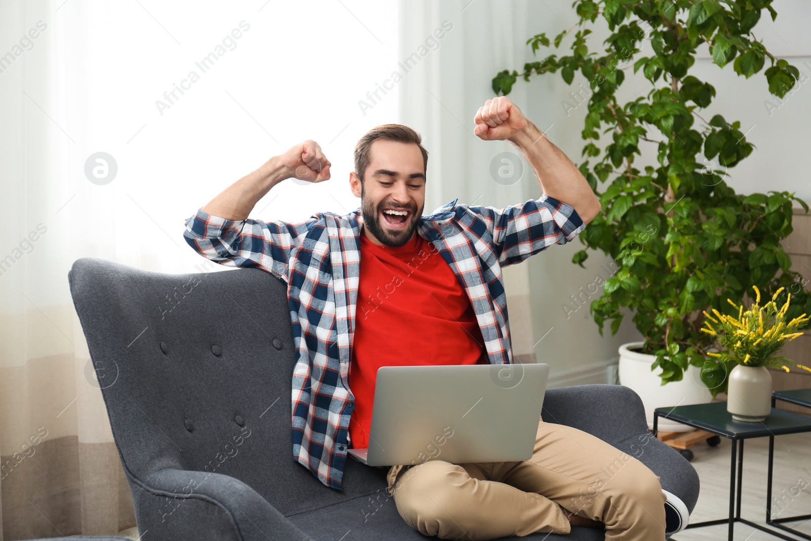 Photo of Emotional young man with laptop celebrating victory on sofa at home