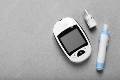 Photo of Glucometer and lancet pen on grey table, flat lay with space for text. Diabetes testing kit