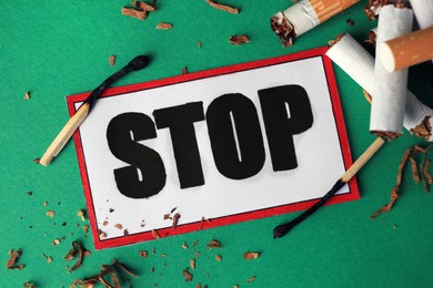 Photo of Stop smoking concept. Card with word Stop, cigarette stubs, tobacco and burnt matches on green background, flat lay