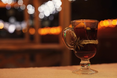 Photo of Glass cup of mulled wine on table against blurred background. Space for text