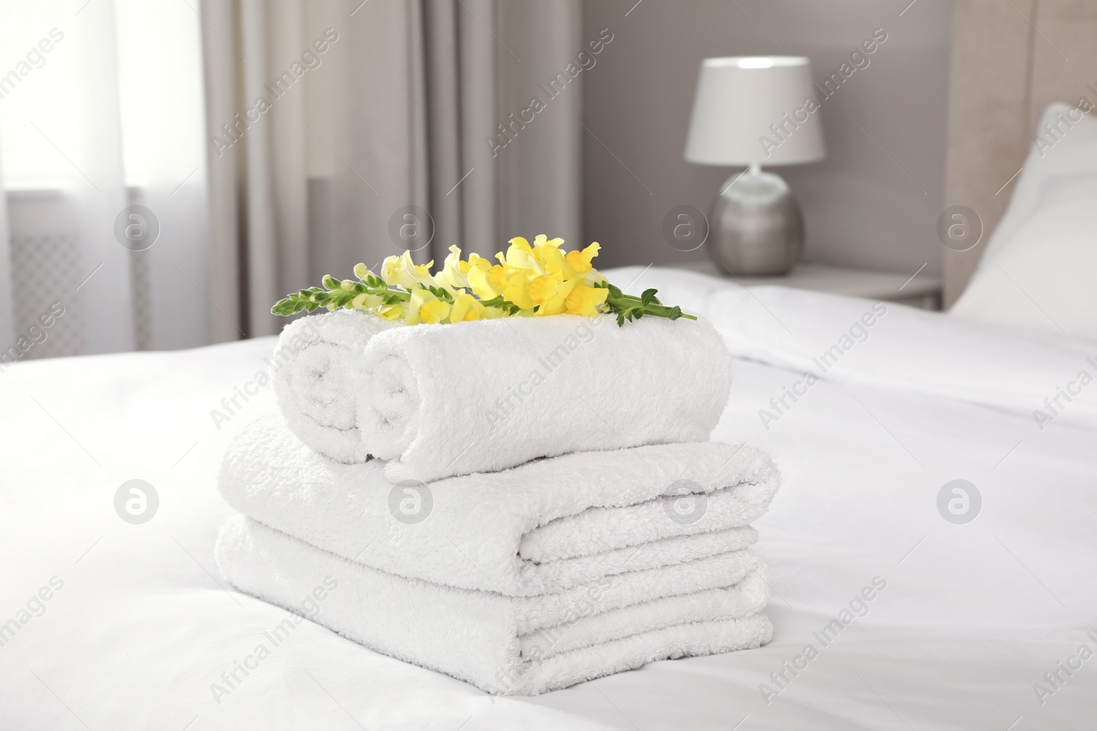 Photo of Fresh white towels with flower on bed indoors