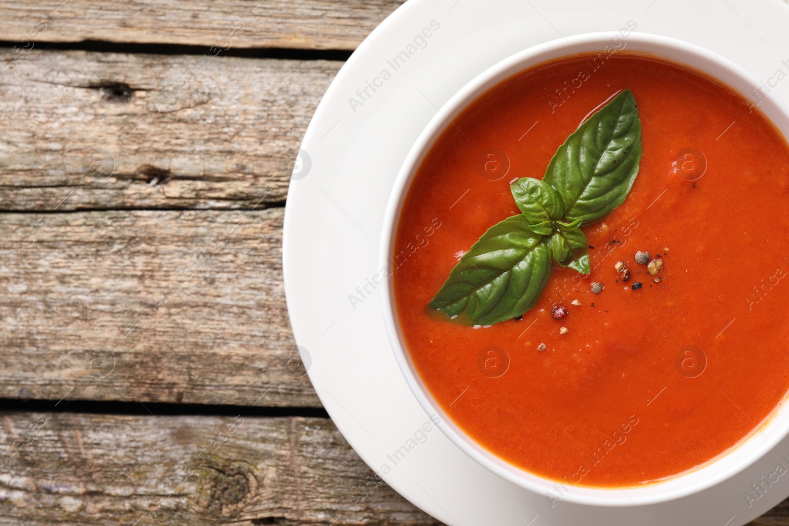 Photo of Delicious tomato soup with basil and spices on wooden table, top view. Space for text