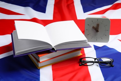 Photo of Learning foreign language. Different books, alarm clock and glasses on flag of United Kingdom