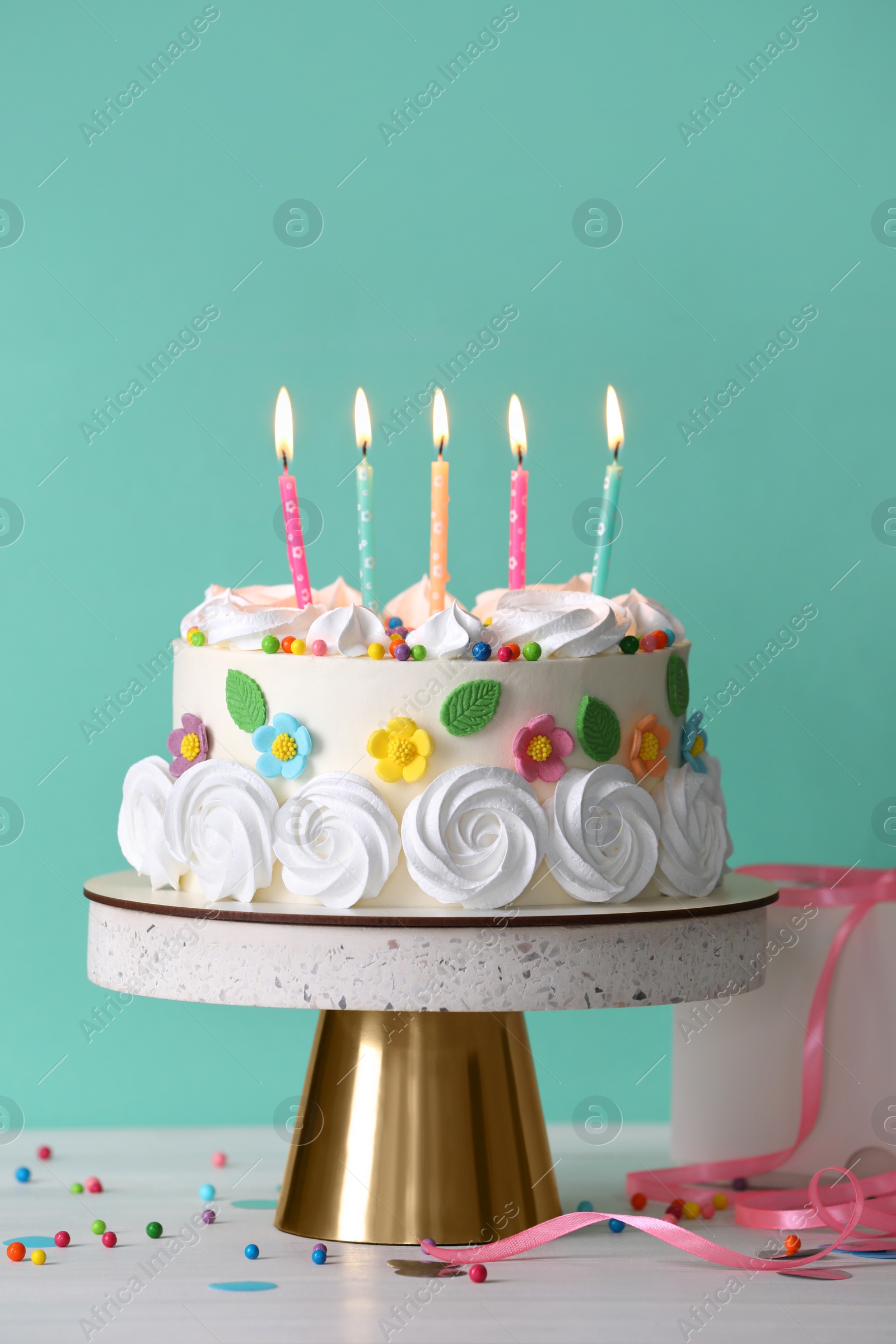 Photo of Delicious birthday cake and party decor on white wooden table against turquoise background