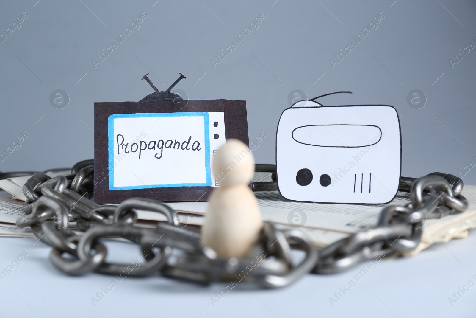 Photo of Propaganda concept. Human mired in media field. Chained wooden figure, newspapers, paper TV and radio on table