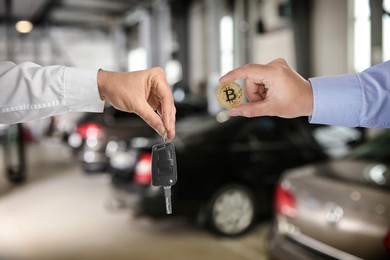 Image of Bitcoin exchange. Man using cryptocurrency to buy auto. Seller holding key and buyer with bitcoin in car dealership, closeup