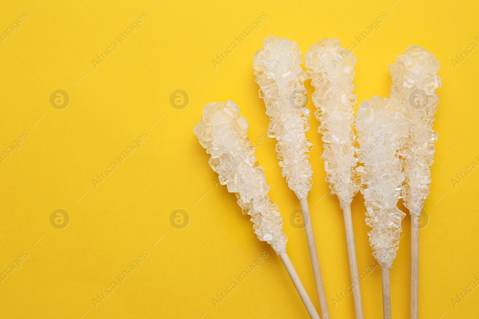 Photo of Wooden sticks with sugar crystals and space for text on yellow background, flat lay. Tasty rock candies