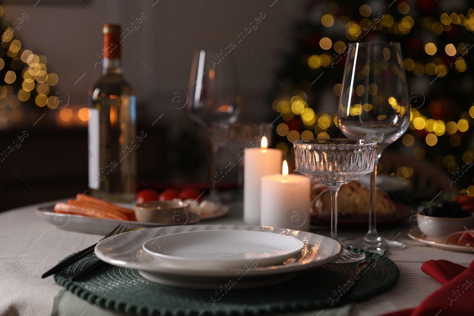 Photo of Christmas table setting with burning candles, appetizers and dishware indoors