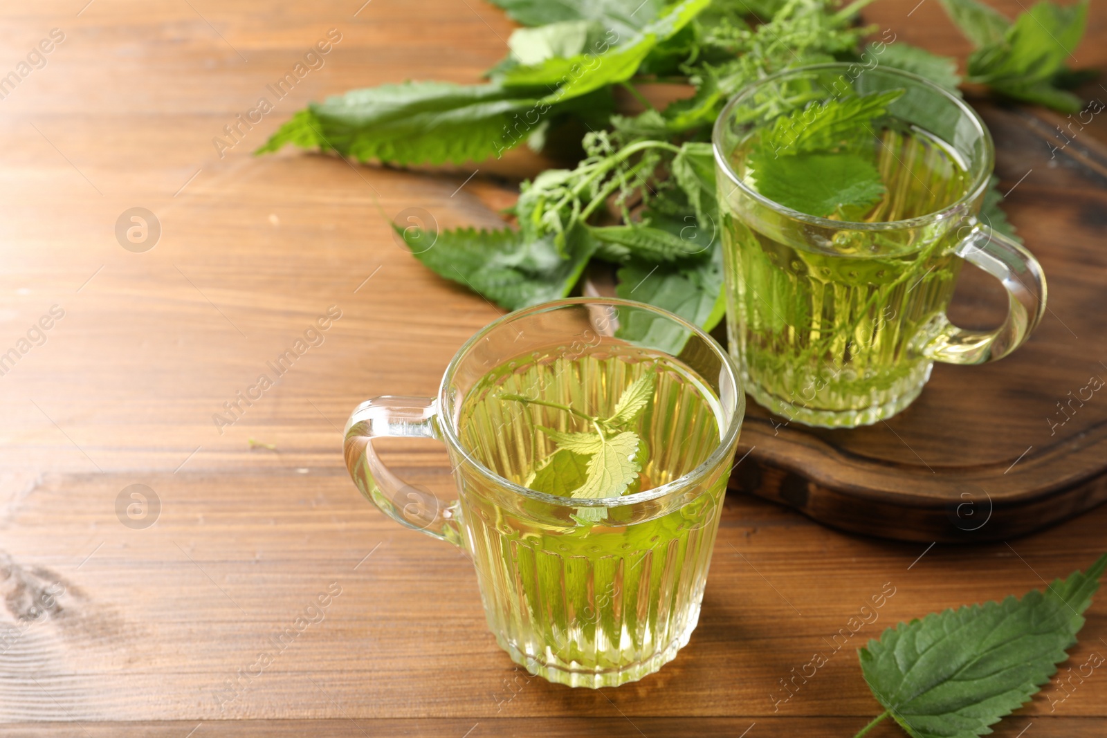 Photo of Aromatic nettle tea and green leaves on wooden table, space for text