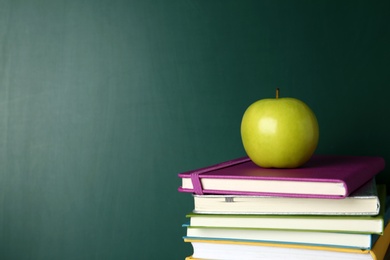 Photo of Books and apple near green chalkboard, space for text. School education