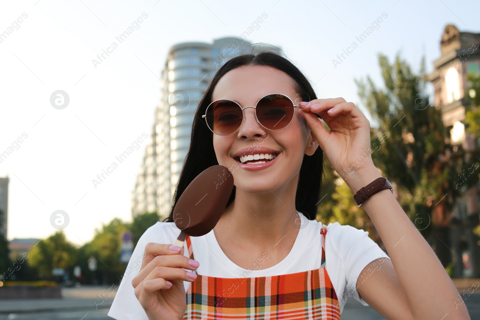 Photo of Beautiful young woman holding ice cream glazed in chocolate on city street