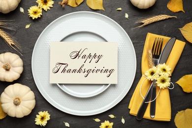 Seasonal table setting with Happy Thanksgiving Day card and pumpkins on dark table, flat lay